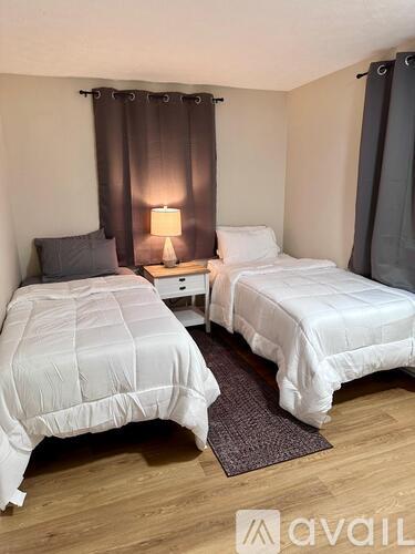 Two beds in a room with wooden floors and a nightstand with a lamp.