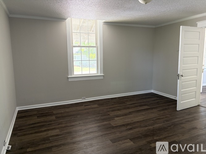 A room with wooden flooring and a window with a view of a building outside.