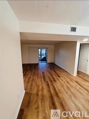 A room with wooden flooring and a window in the distance.