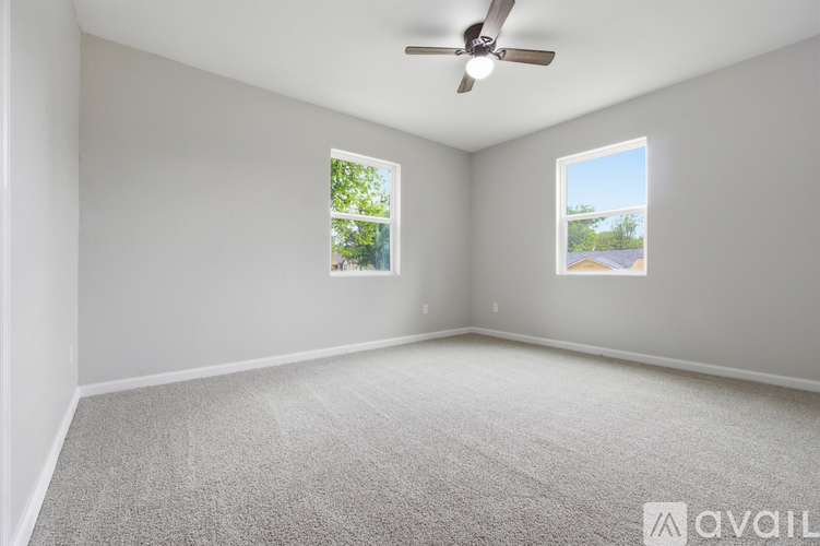 A spacious room with a ceiling fan and two windows.