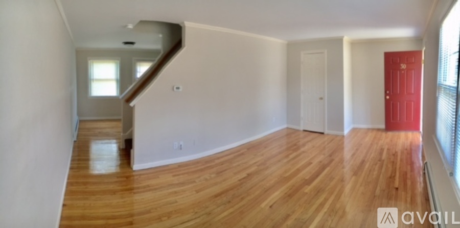 A room with wooden floors and white walls, with a red door on the right side.