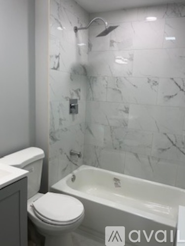 A white toilet sits next to a bathtub in a marble-tiled bathroom.