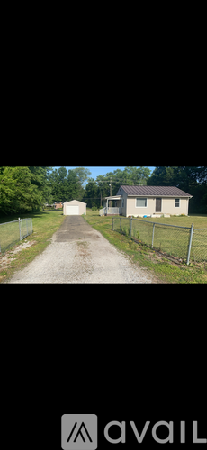 A gravel road leads to a white house with a metal fence on either side.
