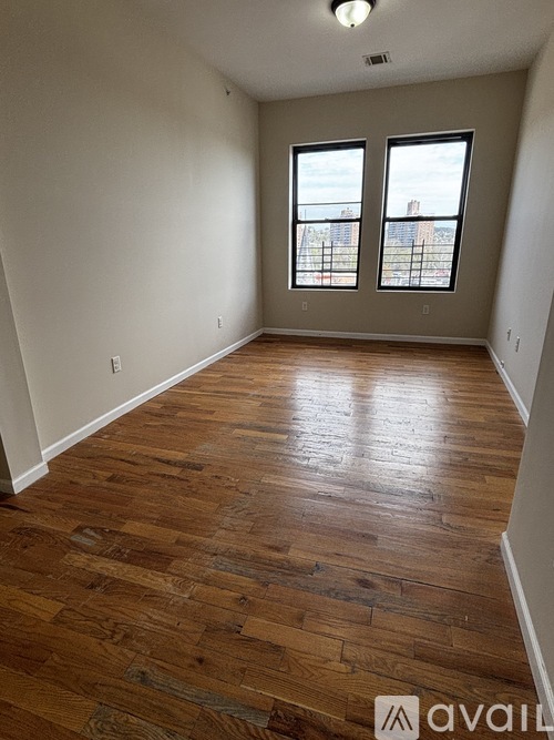 A room with wooden flooring and two windows.
