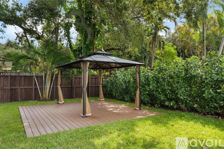 A gazebo is situated in a grassy area with a wooden deck and trees in the background.