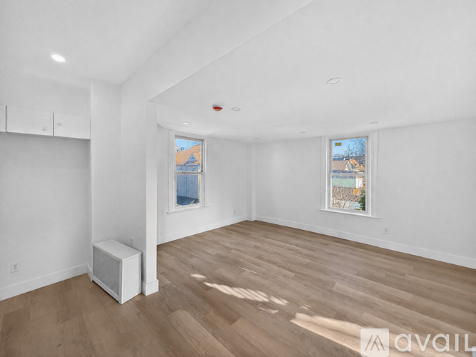 A spacious room with wooden floors and two windows.
