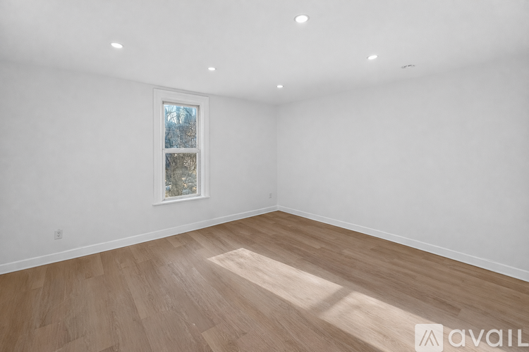 A room with wooden flooring and a window showing trees outside.
