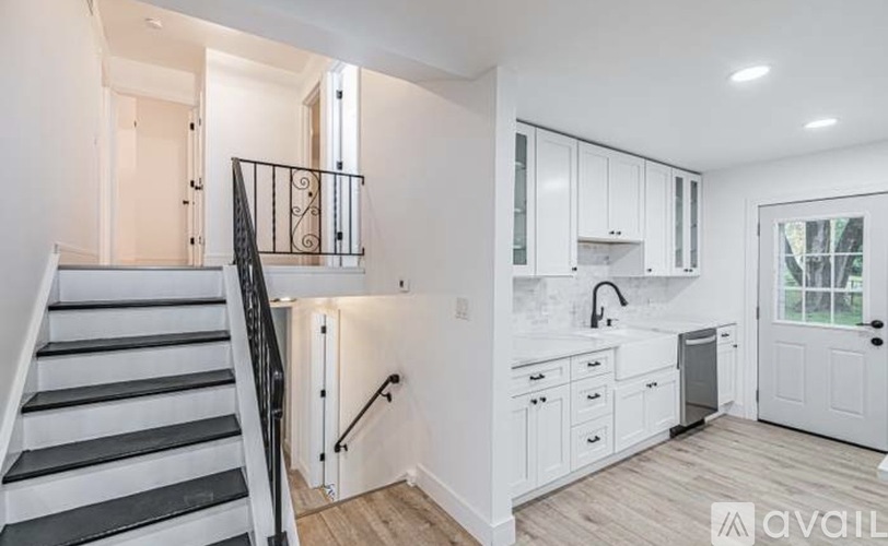 A modern kitchen with white cabinets and a staircase with black railings.