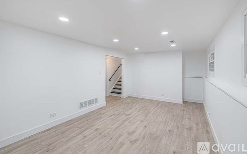 A spacious room with wooden flooring and a staircase in the background.