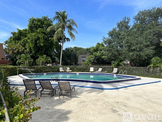 A pool surrounded by chairs and trees.