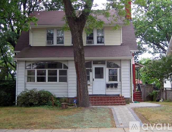 A white house with a brown roof and a tree in front.
