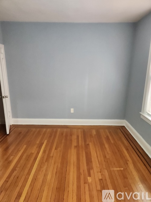 A room with wooden flooring and a door on the left.