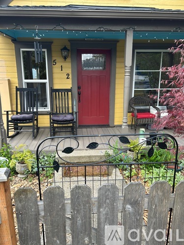 A yellow house with a red door and a black metal table and chairs on the porch.