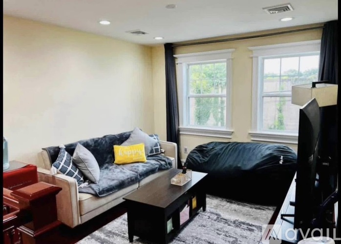 A living room with a grey couch, a black ottoman, and a television.