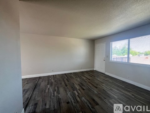 A room with wooden flooring and a window showing trees outside.