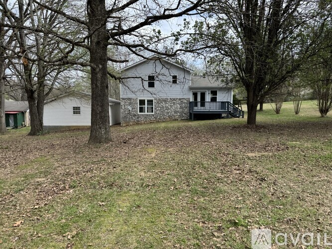 A white house with a grey roof is surrounded by trees and grass.