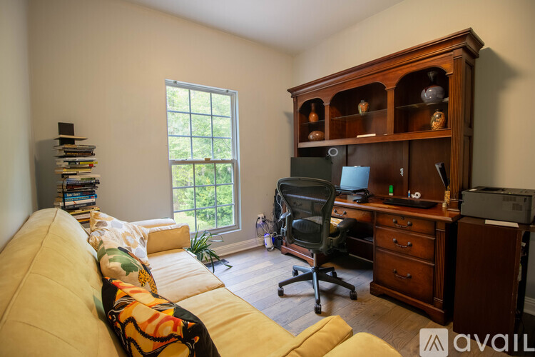 A room with a yellow couch, a desk with a computer, and a window with a view of trees.