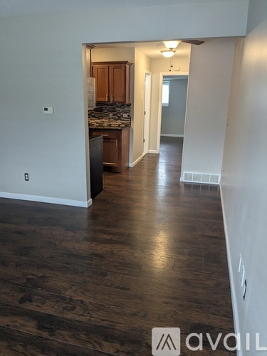 A room with wooden floors and a kitchen area in the background.