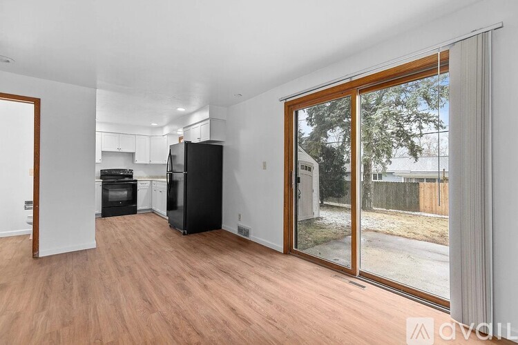 A kitchen with white cabinets and a black fridge is visible through a sliding glass door.