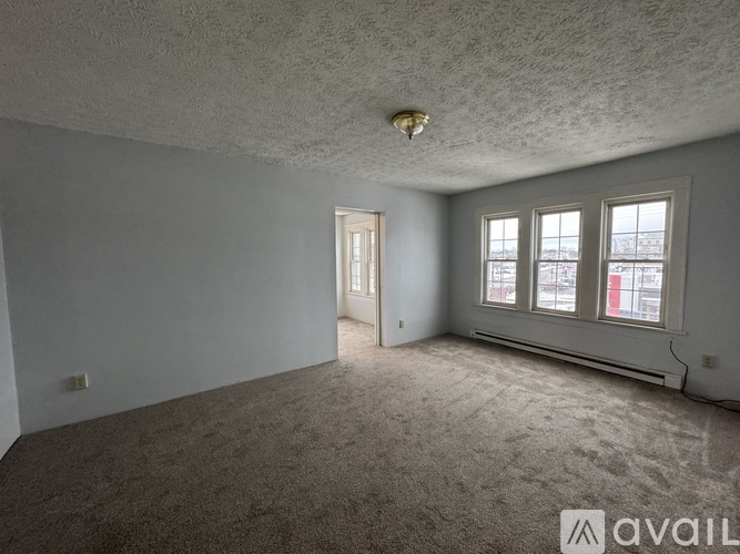 A room with a carpeted floor, a ceiling fan, and a window with a view of a parking lot.