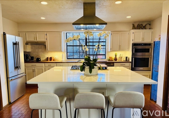 A kitchen with a large island and white chairs.