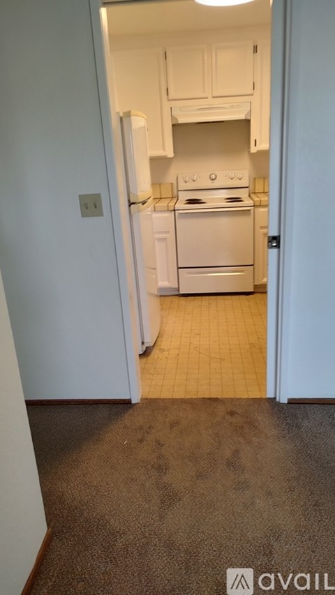 A kitchen with white appliances and cabinets is visible through an open door.
