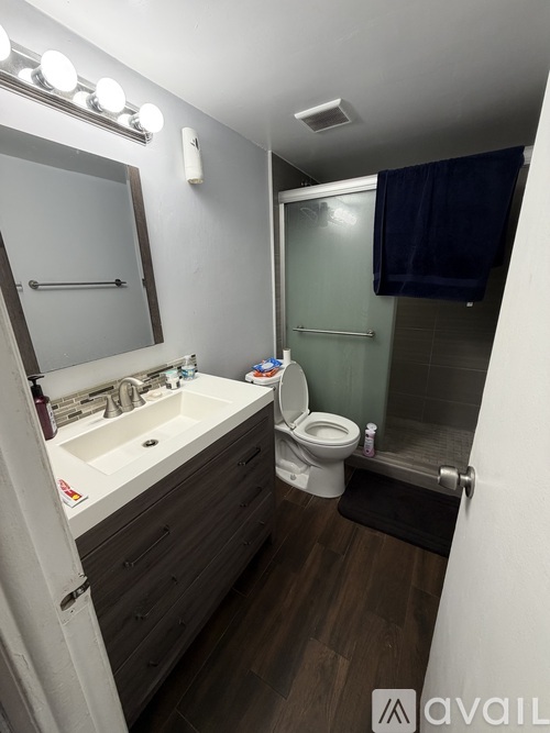 A bathroom with a toilet, sink, mirror, and wooden floors.