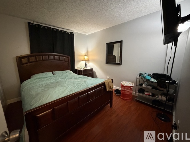 A bedroom with a bed, a nightstand with a lamp, and a TV mounted on the wall.