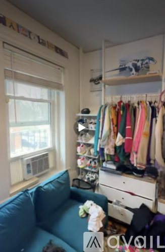 A room with a blue couch and a clothing rack with clothes hanging on it.