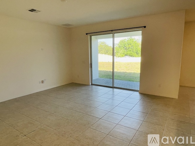 A spacious room with tiled flooring and a sliding glass door leading to a grassy area.