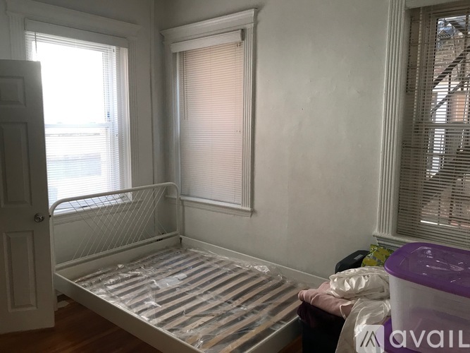 A white bedroom with a metal bed frame and a window with blinds.