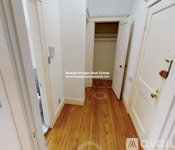 A hallway with wooden floors and white walls leading to a door.