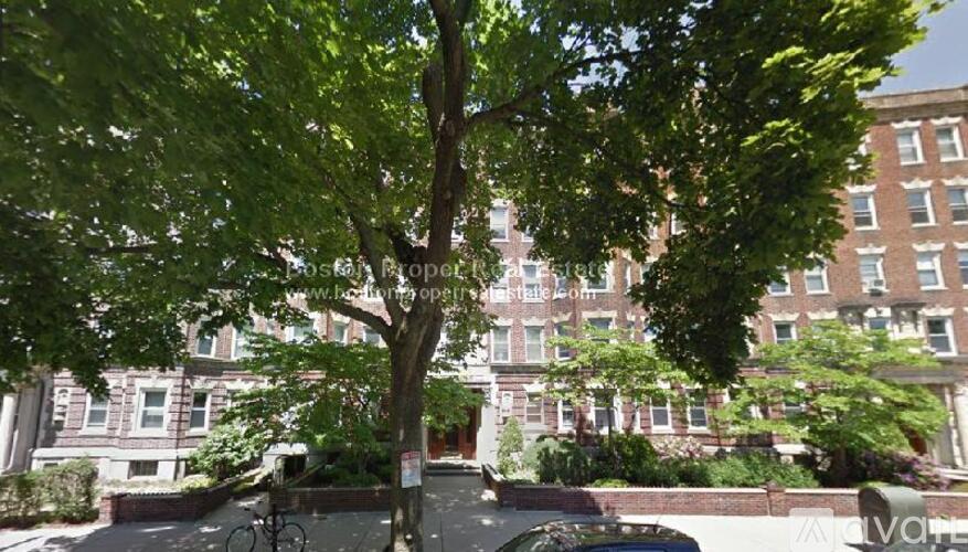 A tree in front of a building with a bicycle parked on the sidewalk.