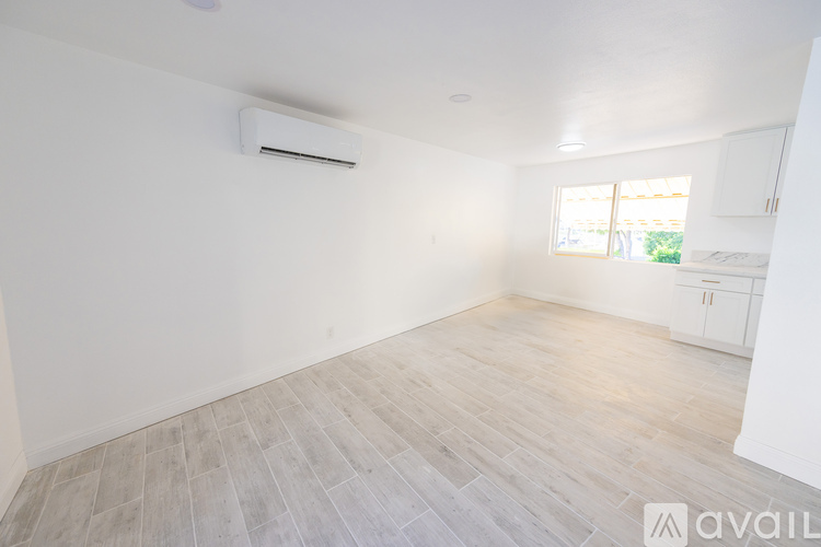 A spacious room with a window, wooden floor, and a wall-mounted air conditioner unit.
