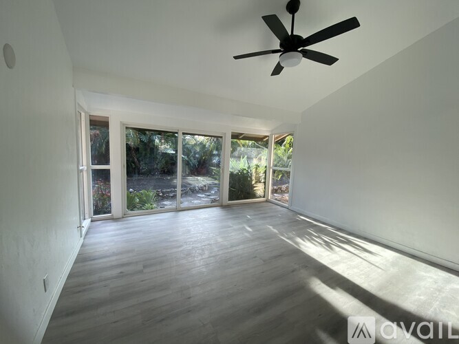 A spacious room with a ceiling fan and sliding glass doors leading to a garden.