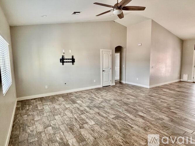 A room with a ceiling fan and light fixture, a door, and a wall-mounted shelf.