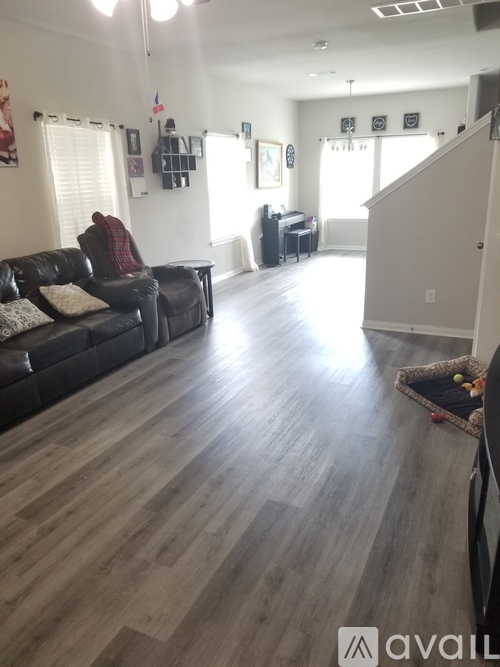 A living room with a black leather couch and wooden flooring.