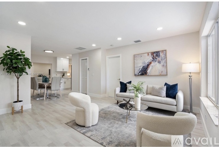 A living room with a white couch, a white chair, a grey rug, and a painting on the wall.