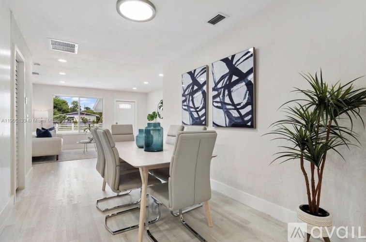 A dining room with a white table and chairs, a potted plant, and a painting on the wall.