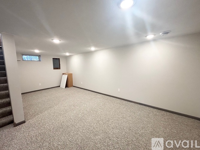 A spacious room with a carpeted floor and a staircase on the left side.