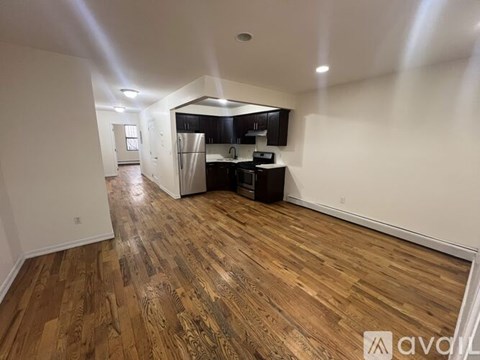 A room with wooden flooring and a kitchen area in the background.