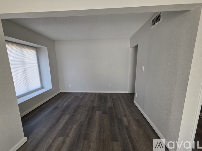 A spacious room with wooden flooring and a window on the left side.
