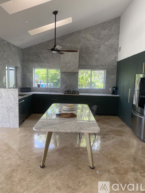 A kitchen with a table in the middle and a fan on the ceiling.