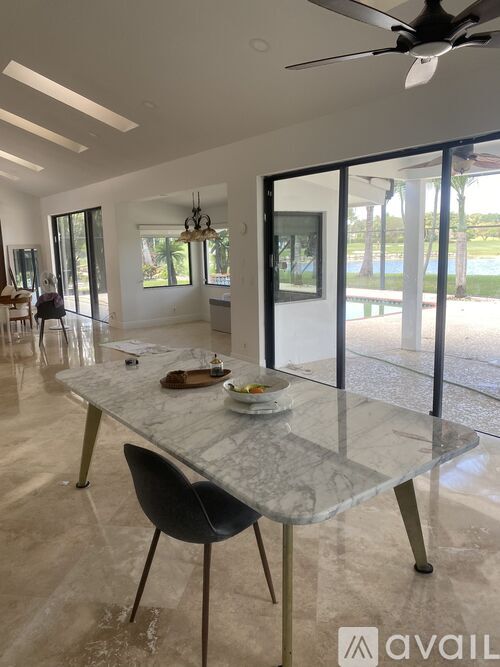 A modern dining room with a marble table and a glass wall leading to a pool.