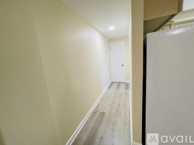 A hallway with a white door and a refrigerator on the right side.