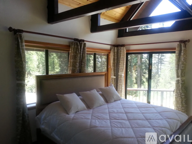 A bedroom with a large bed and a balcony with a view of trees.