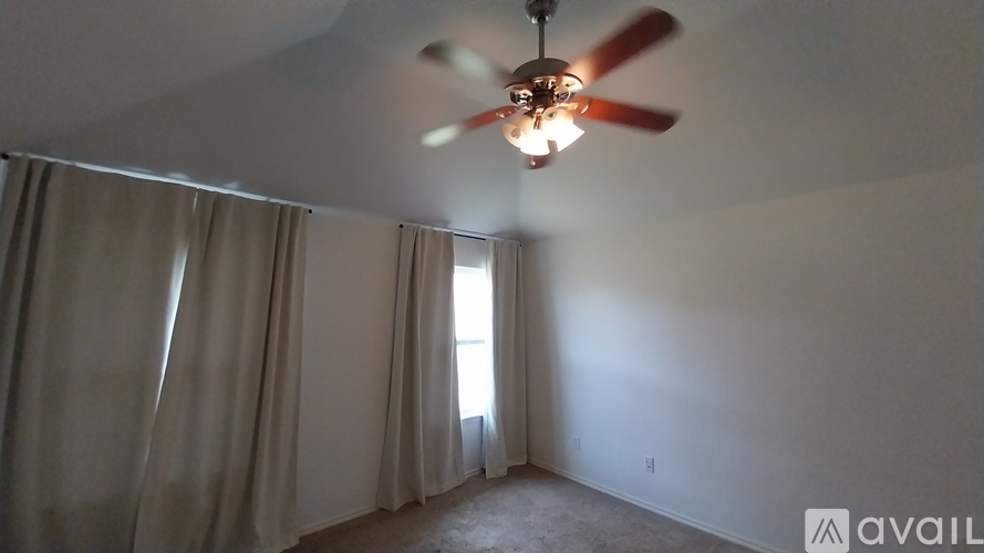 A room with a ceiling fan and a window with curtains.