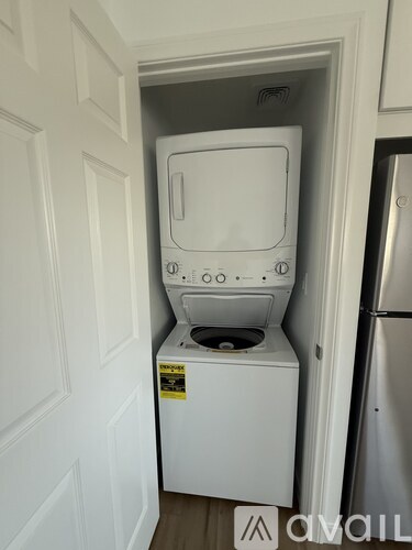 A white washing machine in a small space between a door and a refrigerator.