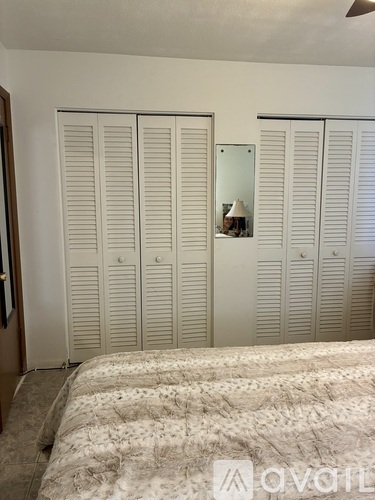 A bedroom with a bed, a mirror, and three white wardrobes.