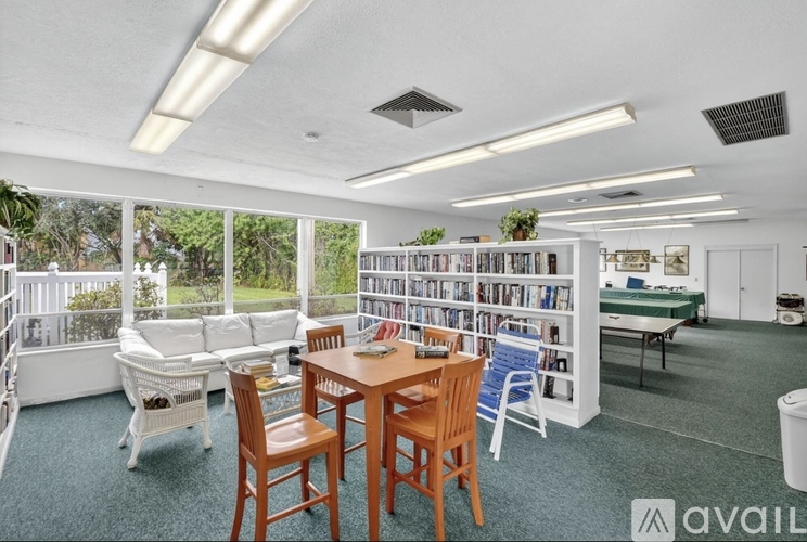 A living room with a dining table and chairs, a sofa, a bookshelf, and a balcony with a view of trees.